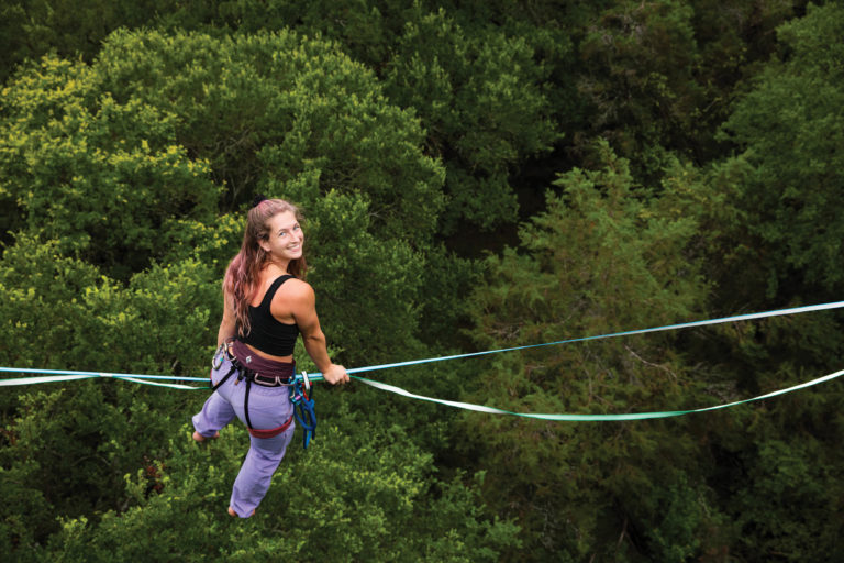 A woman smiling while walking on a slack line.