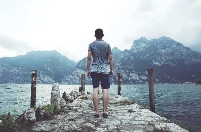 A man standing on a dock looking out at the mountainous landscape.