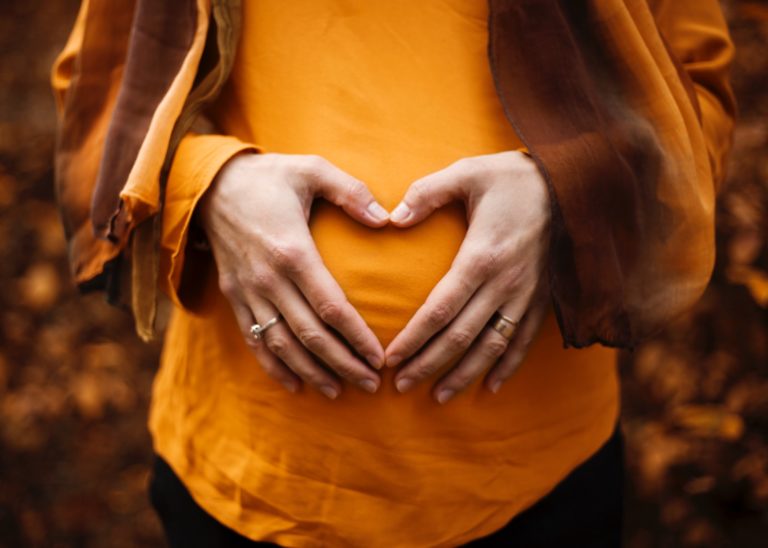 A pregnant woman making a heart with her hands on top of her belly.