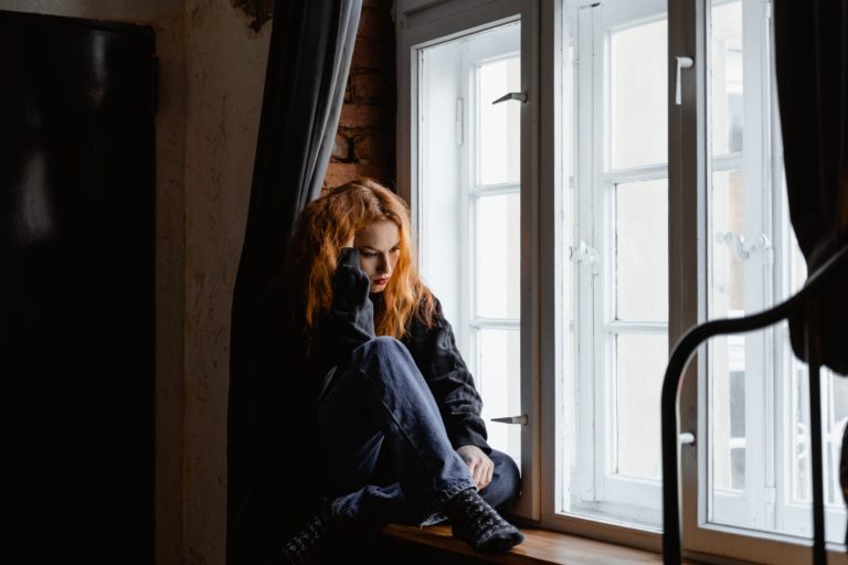 A woman sitting by the window looking sad.