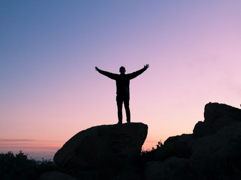 Silhouette of a man raising his hands on top of a mountain.