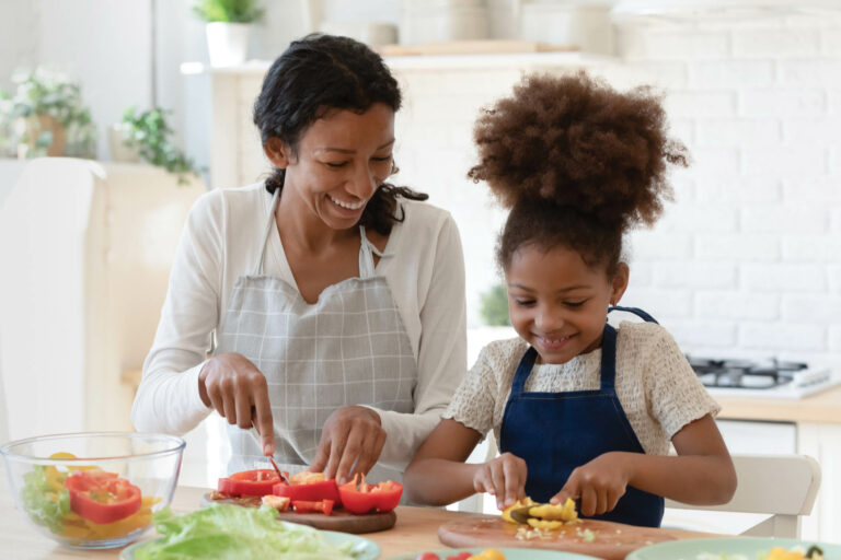 Happy young mixed race woman preparing food with daughter.