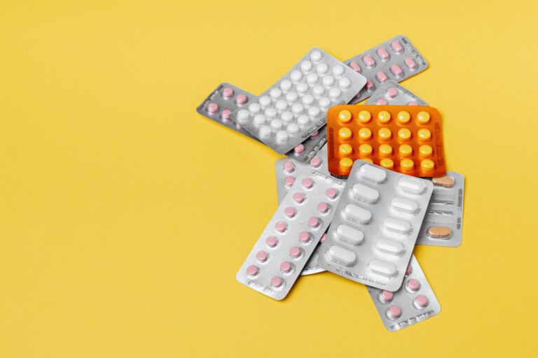 Heap of various pills in blisters on yellow background.