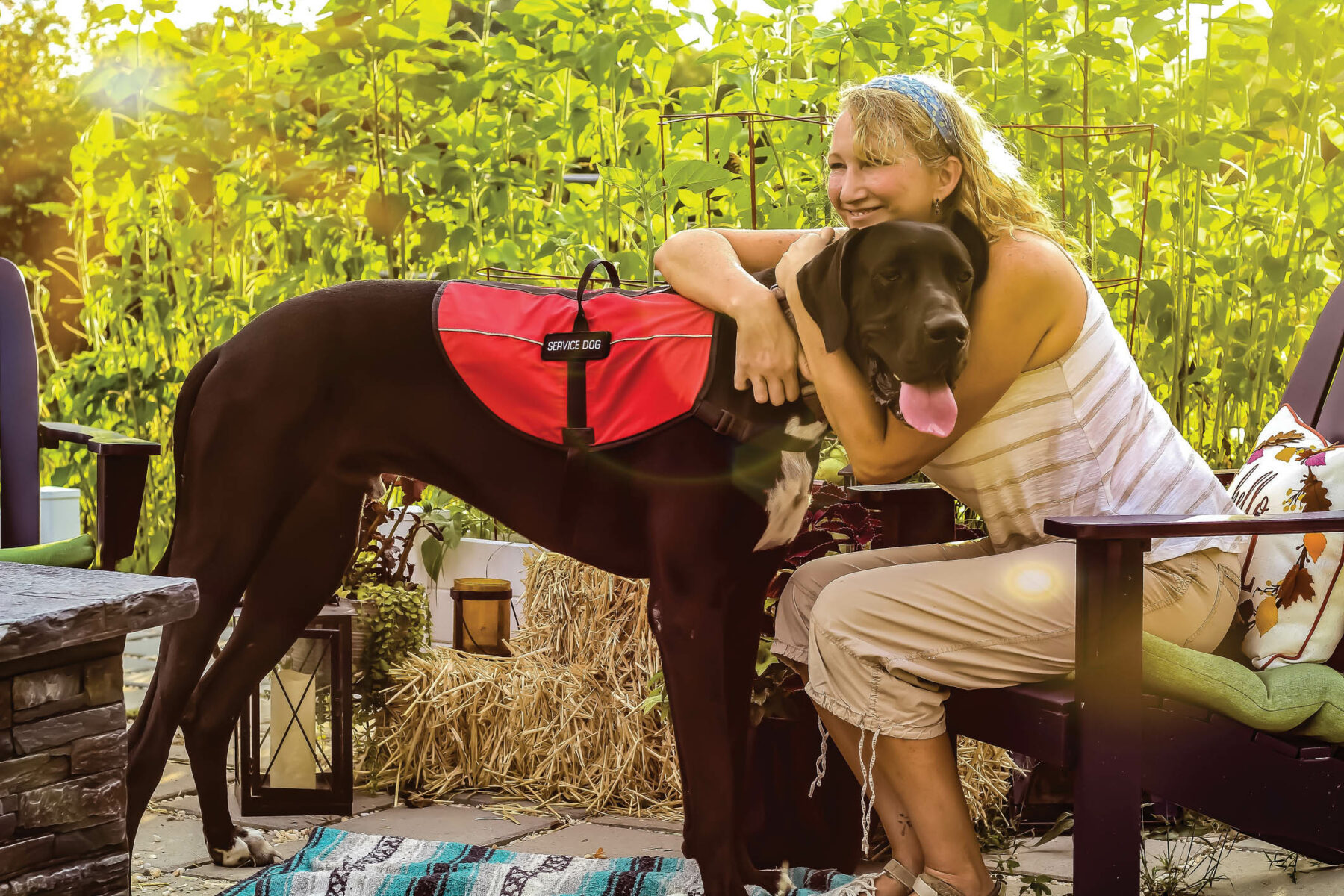 Middle aged woman with mobility issues is able to enjoy her garden patio outdoors with her Great Dane service dog helping her.